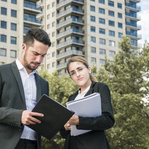 close-up-businessman-businesswoman-holding-documents-standing-front-building